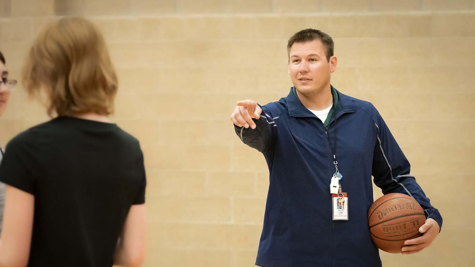 Physical education teacher teaching basketball to high school students
