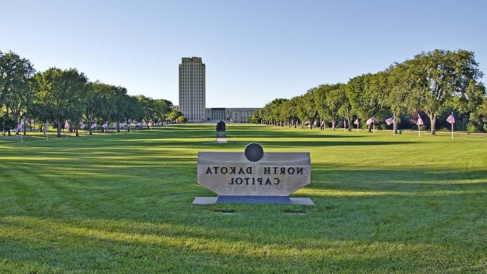 Alt text: A concrete sign for the ND State Capitol is in forefront with the expansive lawn and capitol building in the background. 
